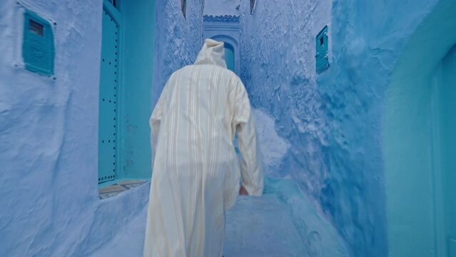 Man with traditional robe walking in the blue streets of Chefchaouen, Morocco