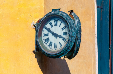 Old round street clock is mounted on a weathered yellow wall . Clock on charming street in a quaint...