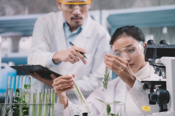 Researcher woman are looking to simple substance in tube on her hands researcher man are standing, looking and taking notes at cosmetic lab and laboratory