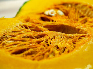 Vivid close-up of thick fresh pumpkin slice on wood table. Smooth orange skin with drops of water glistening on surface. Soft natural light illuminates texture and color of ripe flesh in great detail.