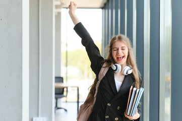 Emotional student girl within walls of institute celebrating successful exam pass, high school or college admission, european employee raised hands feels happy by salary growth, got promoted concept - obrazy, fototapety, plakaty