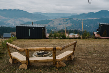 Fire pit, fireplace outdoors. A place with a bonfire in backyard of black house. Cabin terrace with mountain view at sunset. A tiny house on hill perfect. Modern architecture in spring or autumn time. - obrazy, fototapety, plakaty