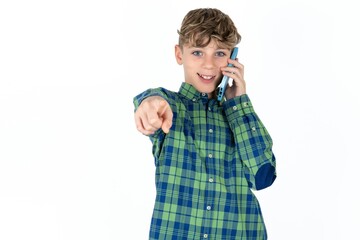 Positive  Caucasian teen boy wearing plaid shirt indicates directly at camera has telephone conversation smiles broadly enjoys talking long hours. You join me