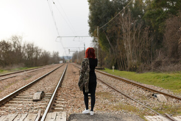 En las vías del tren una mujer caminando con chaqueta militar de espaldas, 