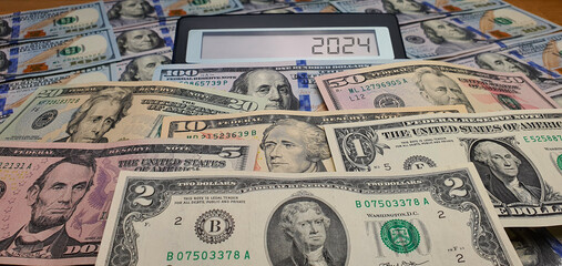 Crisis in the world economy in the new year 2024. Calculator on the background of US dollar banknotes. Europe, recession, inflation, cost of living, war, investments, bills, poverty, infrastructure