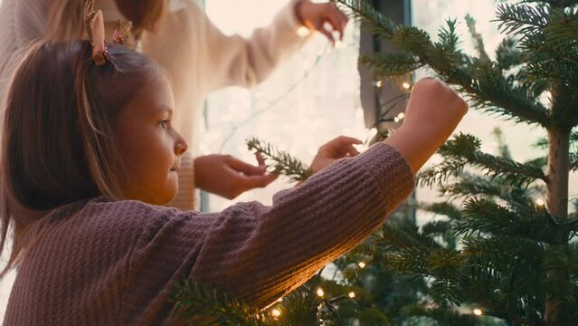 Cheerful mother and daughter decorating Christmas tree with lights. Shot with RED helium camera in 8K.