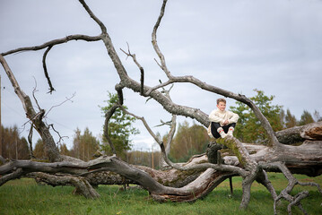 Portrait of boy teenager sitting on a dead tree branch in autumn park