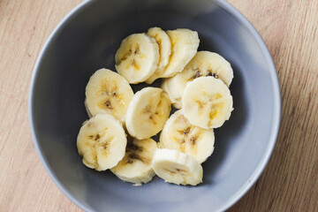 Top view banana salad. Blue ceramic bowl with fruit slices inside. Banana slices in bowl. Wooden table healthy breakfast. Banana pieces background.