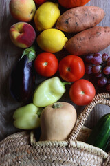  Round straw bag with seasonal fruit and vegetable on wooden background. Late summer or early autumn. Top view.