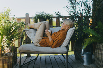 Beautiful woman relaxing in the garden, sitting on patio chair and drinking cup of coffee. Mother having moment to herself while her child is sleeping.