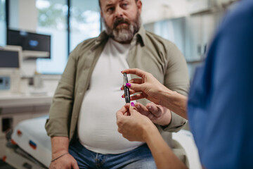 Nurse checking man's blood glucose level using a fingerstick glucose meter. Obese, overweight man is at risk of developing type 2 diabetes. Concept of health risks of overwight and obesity. - obrazy, fototapety, plakaty