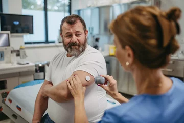 Fotobehang Doctor applying a continuous glucose monitor sensor on patient's arm. Obese, overweight man is at risk of developing type 2 diabetes. Concept of health risks of overwight and obesity. © Halfpoint