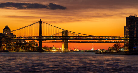 Fiery sunset with Manhattan Bridge and Brooklyn Bridge with illuminated Statue of Liberty. New York City