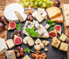 Variety of sliced cheeses with fruits, mint, nuts and cheese cutting knives. - obrazy, fototapety, plakaty