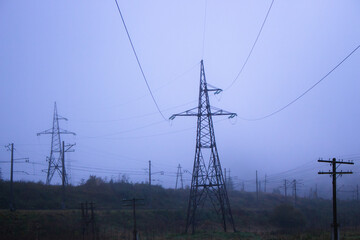 Power lines in foggy morning in autumn field. Electrical industry concept. Electricity equipment in...