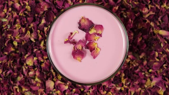 Rose moon milk in glass, top view. Ayurveda warm drink consumed before bed. Nice in case of sleeplessness. Midnight relaxing drink. Rose petals background. Video, 4K, Rotating.