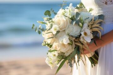 Close-up view of a bride holding a wedding floral bouquet on sand beach. Summer tropical vacation concept.