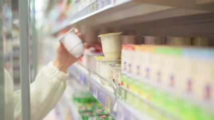 The hands of a girl-buyer take a container with a dairy product from the shelf