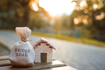 Bridge loan concept - is a short-term loan secured by real estate. Money bag and miniature house in...