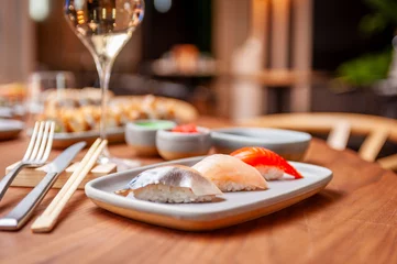 Tuinposter Nigiri set: mackerel, sea bass, salmon on a plate on a table in a sushi bar © nik0s