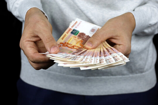 Russian rubles in male hands, cash pay, salary or bribe concept. Man in sweater holding paper currency of Russia
