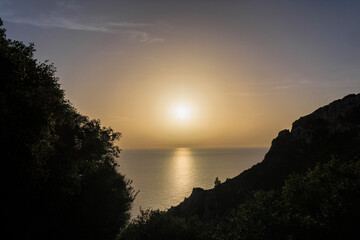 The sun sets golden over the sea against the silhouette of the coast at the ruins of Angelokastro near Agios Spiridon on the island of Corfu
