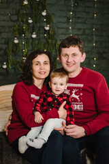 Mom and dad hug son enjoy time together. Young family sitting in bed near Christmas tree at home. Merry Christmas and happy winter holidays. Mother, father embrace child. Decorated interior of a house