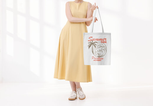 Mockup of woman in dress holding customizable tote bag on finger