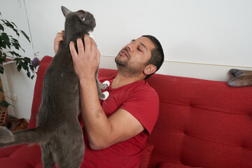 Man on Sofa Engaging Playfully with Gray Cat