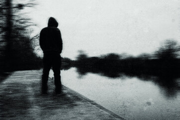 A spooky mysterious hooded figure looking at a river. On a bleak winters day. With an abstract, grunge, blurred edit.