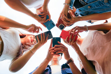Image of a group of young Asian people laughing together and using their phones - obrazy, fototapety, plakaty