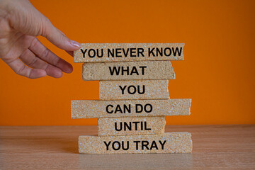 Concept words You never know what you can do until you try. Words on brick blocks. Beautiful wooden table orange background. Businessman hand