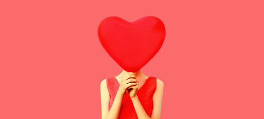 Woman covering her head with big red heart shaped balloon on pink background