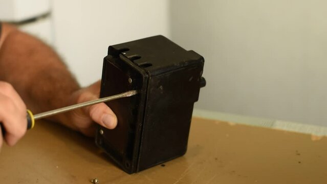 The electrician installs the bolt into the hole with his hands, and then tightens it with a screwdriver.