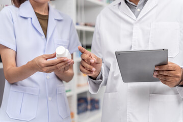 Close up of asian male pharmacist and coworker wearing lab coat and checking medicine product stock with database tablet in the pharmacy drugstore.
