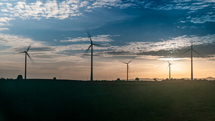 Erneuerbare und nachhaltige Energieerzeugung mit rotierenden Windrädern, abends im Gegenlicht auf...