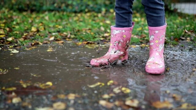 Child wearing pink rain boots with unicorns and jumping in puddle on a fall day