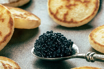 Silver spoon with caviar closeup with blinis, an elegant festive appetizer, luxury food