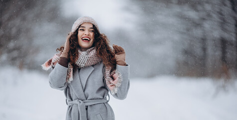 Fototapeta na wymiar Beautiful smiling young woman in wintertime outdoor. Winter concept. Walking in snowy forest.