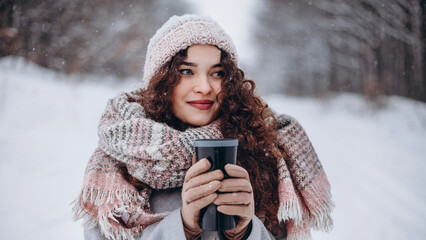 A girl holding a thermos with a hot drink. A mug of coffee in her hands. Winter atmosphere.