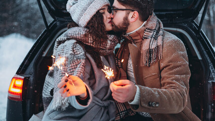 Romantic couple in love celebrate together the new year with fire sparkler at the back of car. Love...