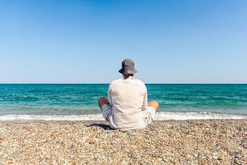 A man sits on the beach in the lotus position and looks at the sea. Meditating man in summer...