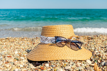 A hat and sunglasses lie on a pebble beach. A hat and sunglasses lie on the shore of the Mediterranean Sea.