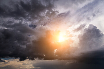 Fototapeta premium Epic Dramatic storm sky with sun. Dark grey black cumulus rain clouds with orange yellow light and sunlight, thunderstorm