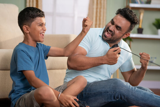 Focus on kid, cheerful indian father and son celebrating win while playing video game by using joystick at home - concept of Joyful gaming, family Fun and weekend activities.