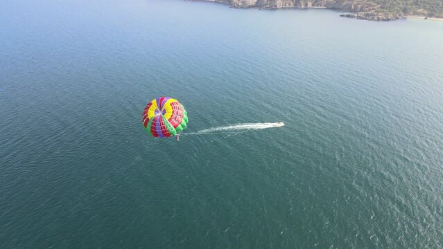 Aerial video of a person parasailing with a boat next to the sea shore