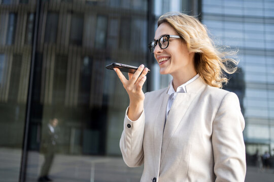 A business woman portrait dictates a voice message in her phone, uses a messenger to communicate with a colleague online. Convenient communication with a partner.