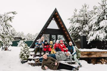 Big family with kids on terrace of mountain country house in snow forest together. Best friends in casual clothes spend winter holidays at cottage. Company people childs on vacation celebrate New Year