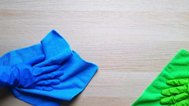 Two hands in rubber gloves wipe the table with microfiber cloths.  Cleaners in blue and green gloves with towels do cleaning. Cleaning company or janitor service. Routine everyday housework.
