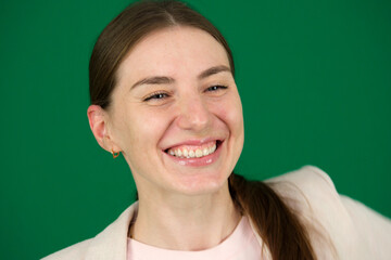 on a green background, chromakey, close-up of a woman with emotions in a beige jacket, red manicure, blue eyes Young woman doing gestucilation wiyh her face, her show teeth. High quality photo